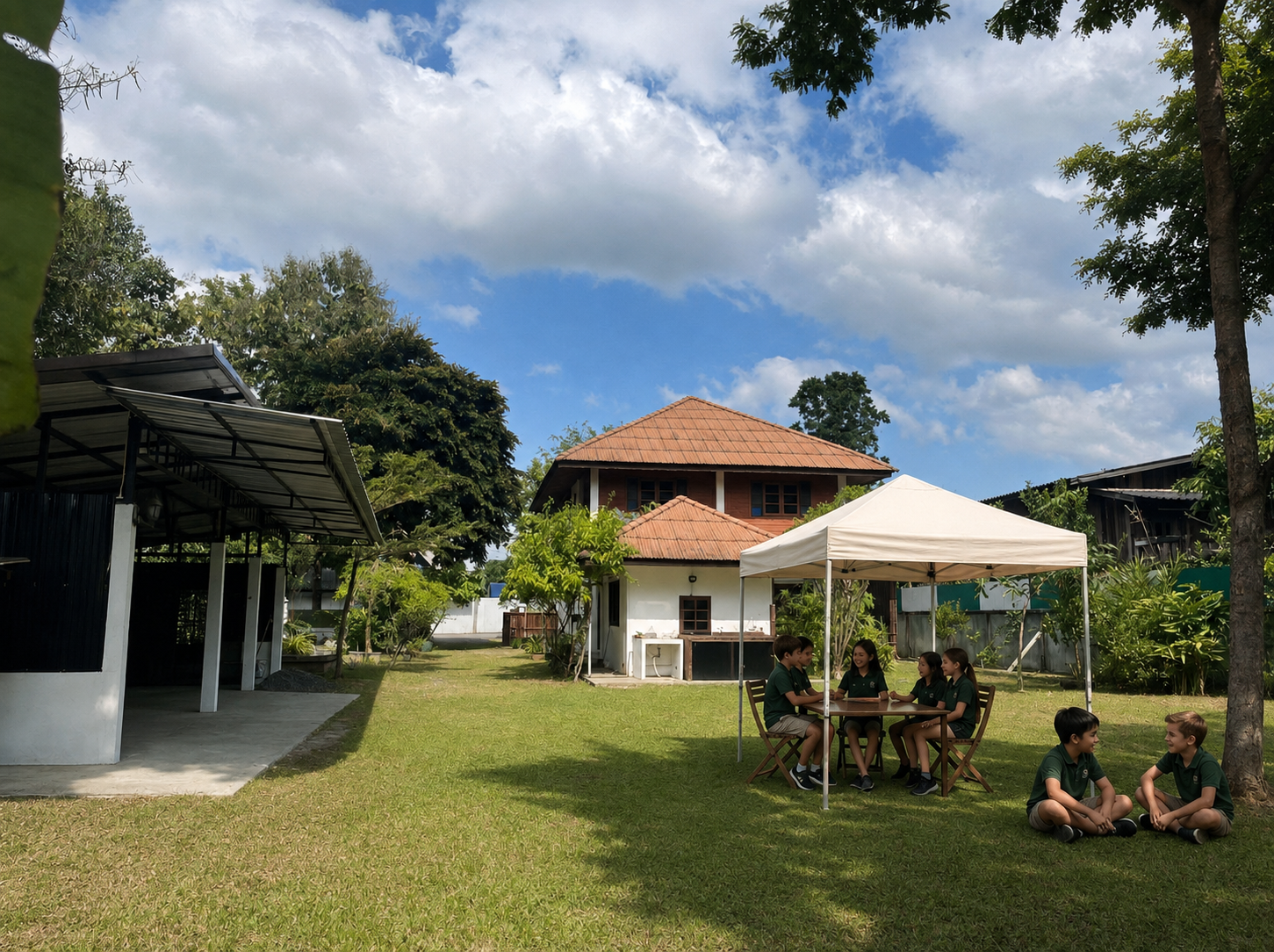Learners socializing beneath a white canopy and in the shade beside the Lanna-style house